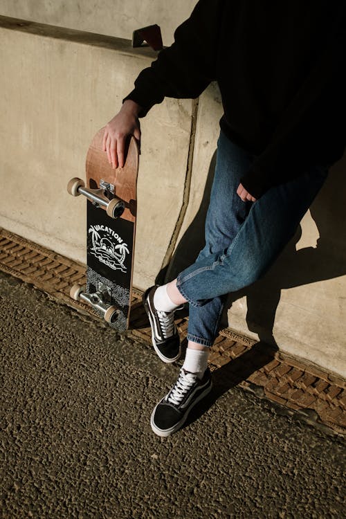 Person in Blue Denim Jeans and Black and White Nike Sneakers Sitting on Brown Wooden Bench