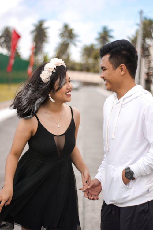 Happy young ethnic female in black dress standing on street with boyfriend and laughing on sunny day