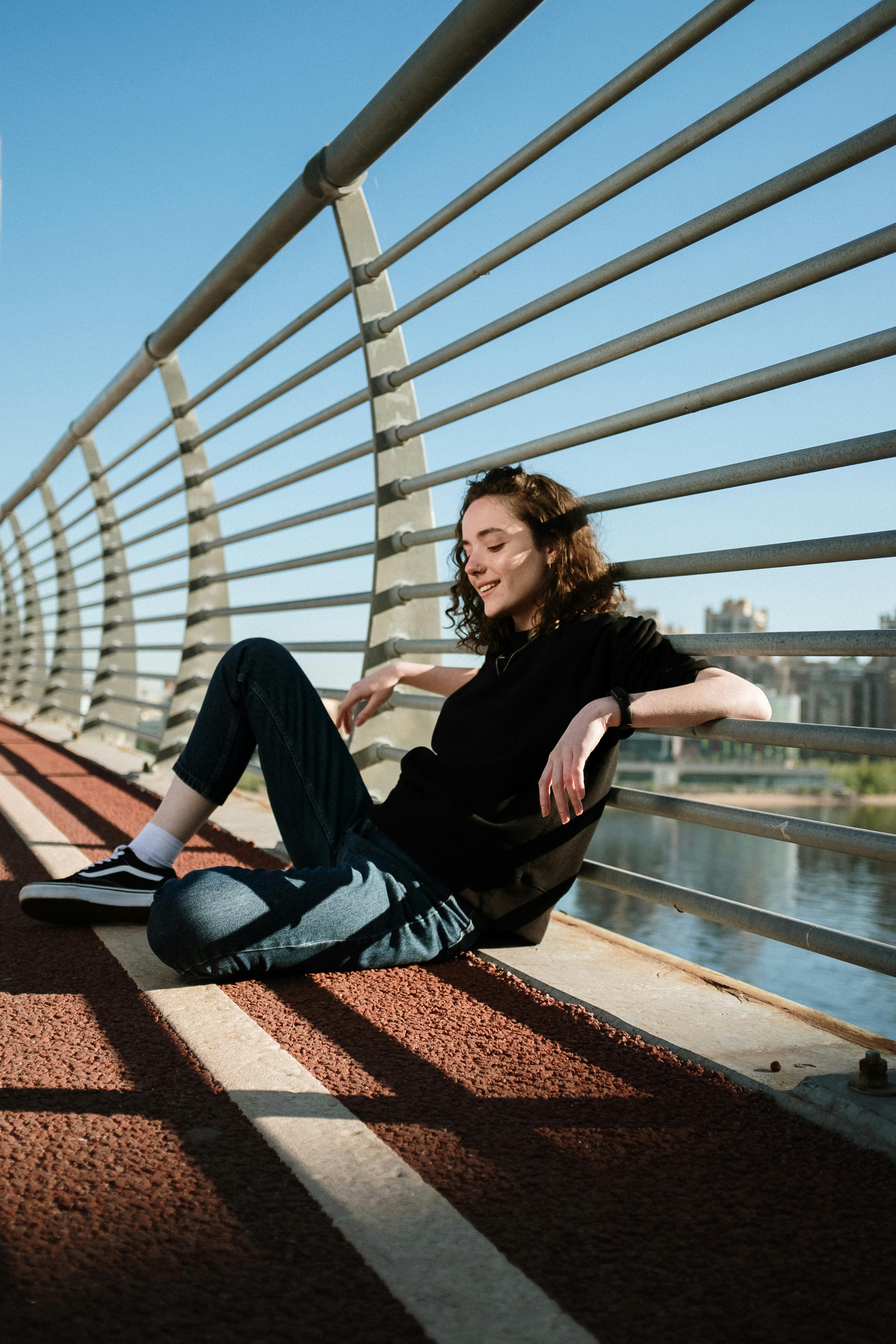 一位年轻女子轻松地坐在桥上，沐浴着水道上的阳光，尽显城市宁静
