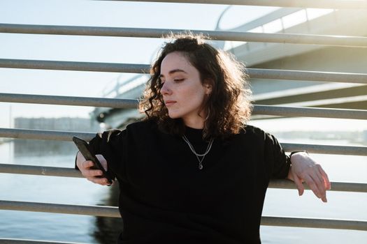 一位轻松的女人靠着手机，倚在铁路边的水与桥上，沐浴在阳光下