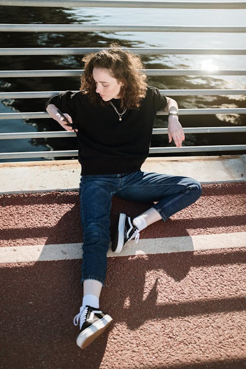 Woman in Black Long Sleeve Shirt and Blue Denim Jeans Sitting on White Bench