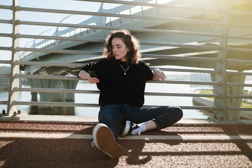 Woman in Black Long Sleeve Shirt and Blue Denim Jeans Sitting on Bench