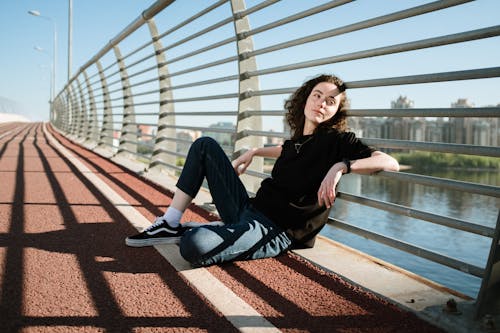 Woman in Black Long Sleeve Shirt and Blue Denim Jeans Sitting on Brown Concrete Floor