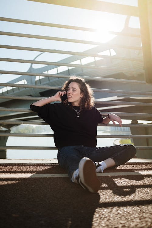 Woman in Black Long Sleeve Shirt and Blue Denim Jeans Sitting on Brown Wooden Bench