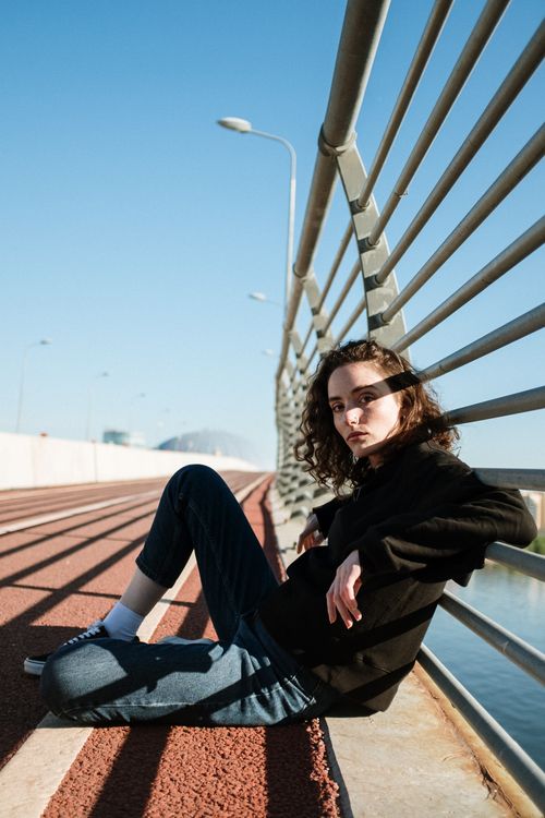 Free A young woman sitting on a bridge with striking shadows and modern urban design. Stock Photo