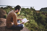A Man Sitting on the Rock while Reading a Book
