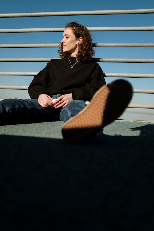 Woman in Black Jacket and Blue Denim Jeans Sitting on Bench