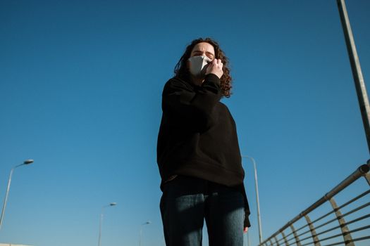 城市桥上，一位戴着面具的女人站在湛蓝的天空下
