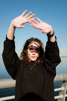 一位身着黑色运动衫、卷发的女士在户外用手遮挡阳光