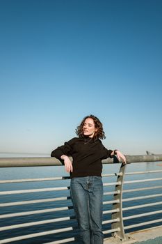 一个女人站在城市河边的护栏旁，享受着晴朗的一天