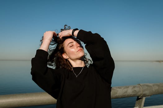A serene moment captured of a woman with curly hair enjoying the outdoors by the water.