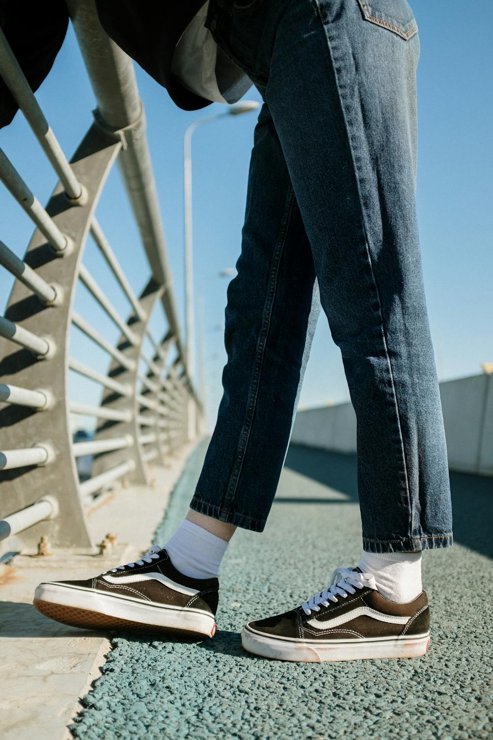 Person in Blue Denim Jeans and Black and White Sneakers Standing on ...