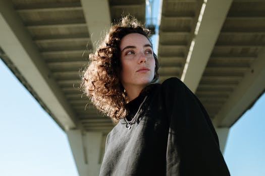 一位卷发的年轻女子在现代风格的桥下，看起来正在沉思