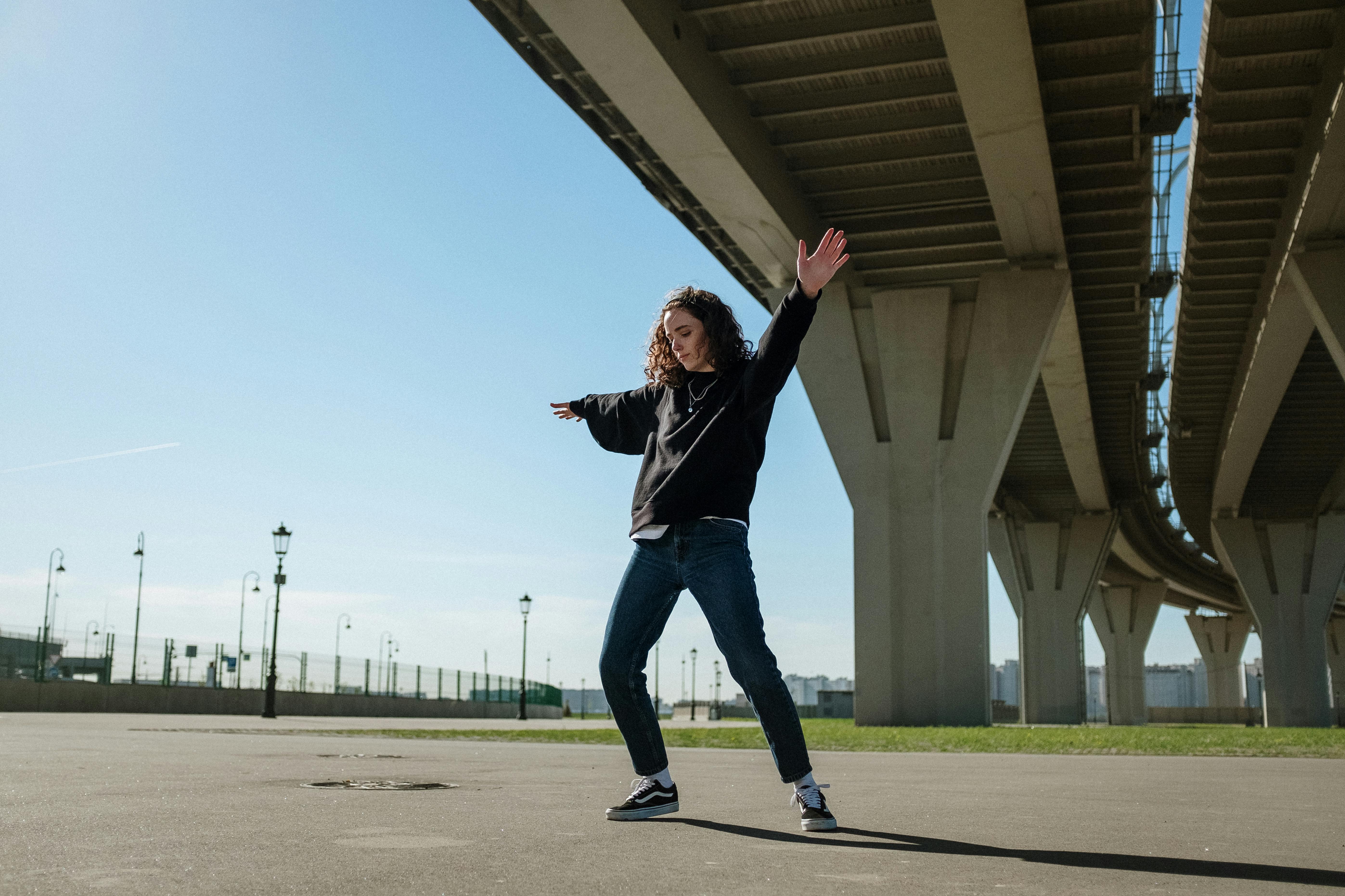 Man in Black Jacket and Blue Denim Jeans Jumping on Green Grass Field