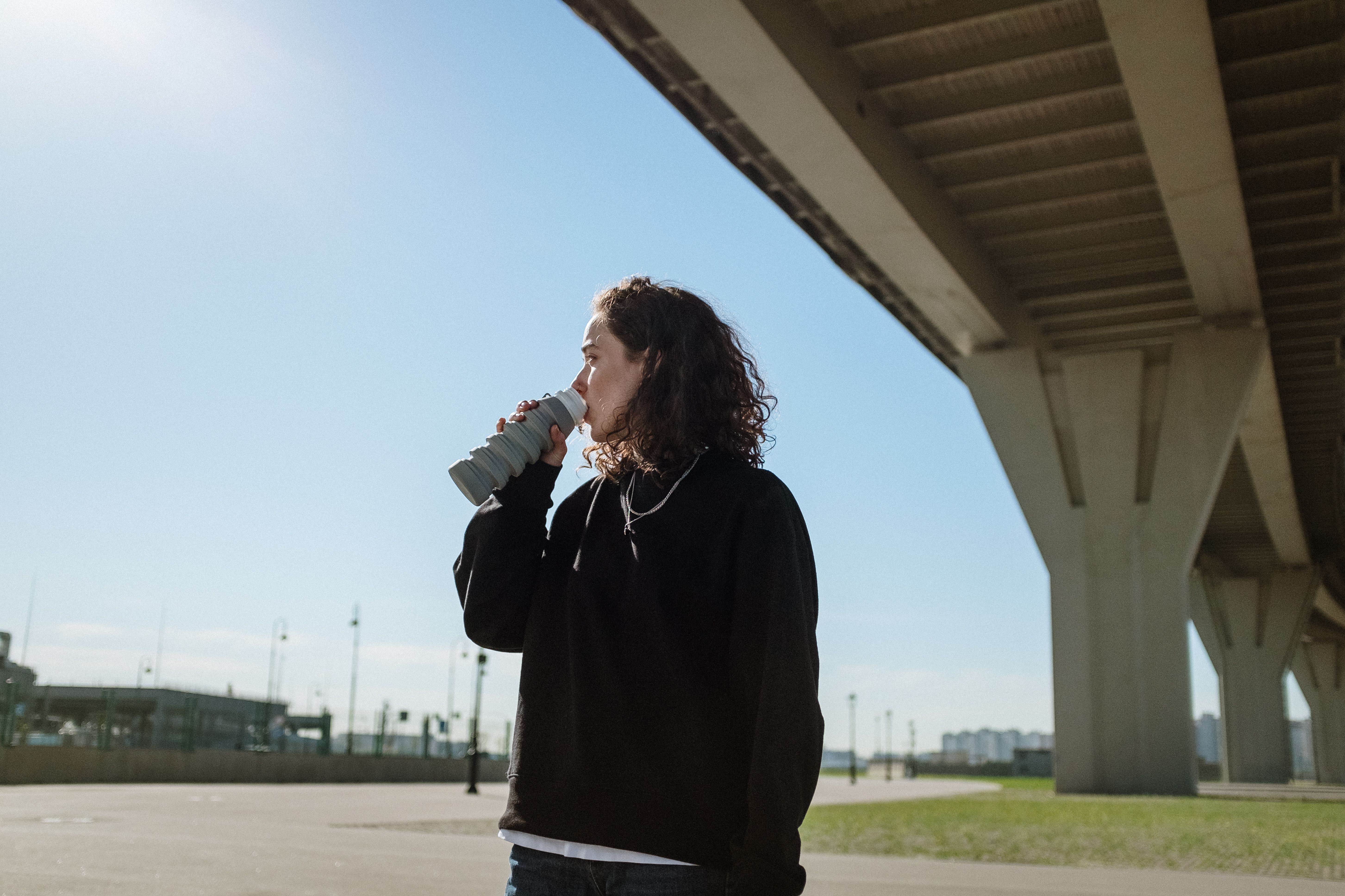 在一个阳光明媚的日子里，一个年轻女子在大城市的桥下从一个水瓶里喝水