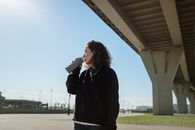 在一个阳光明媚的日子里，一个年轻女子在大城市的桥下从一个水瓶里喝水