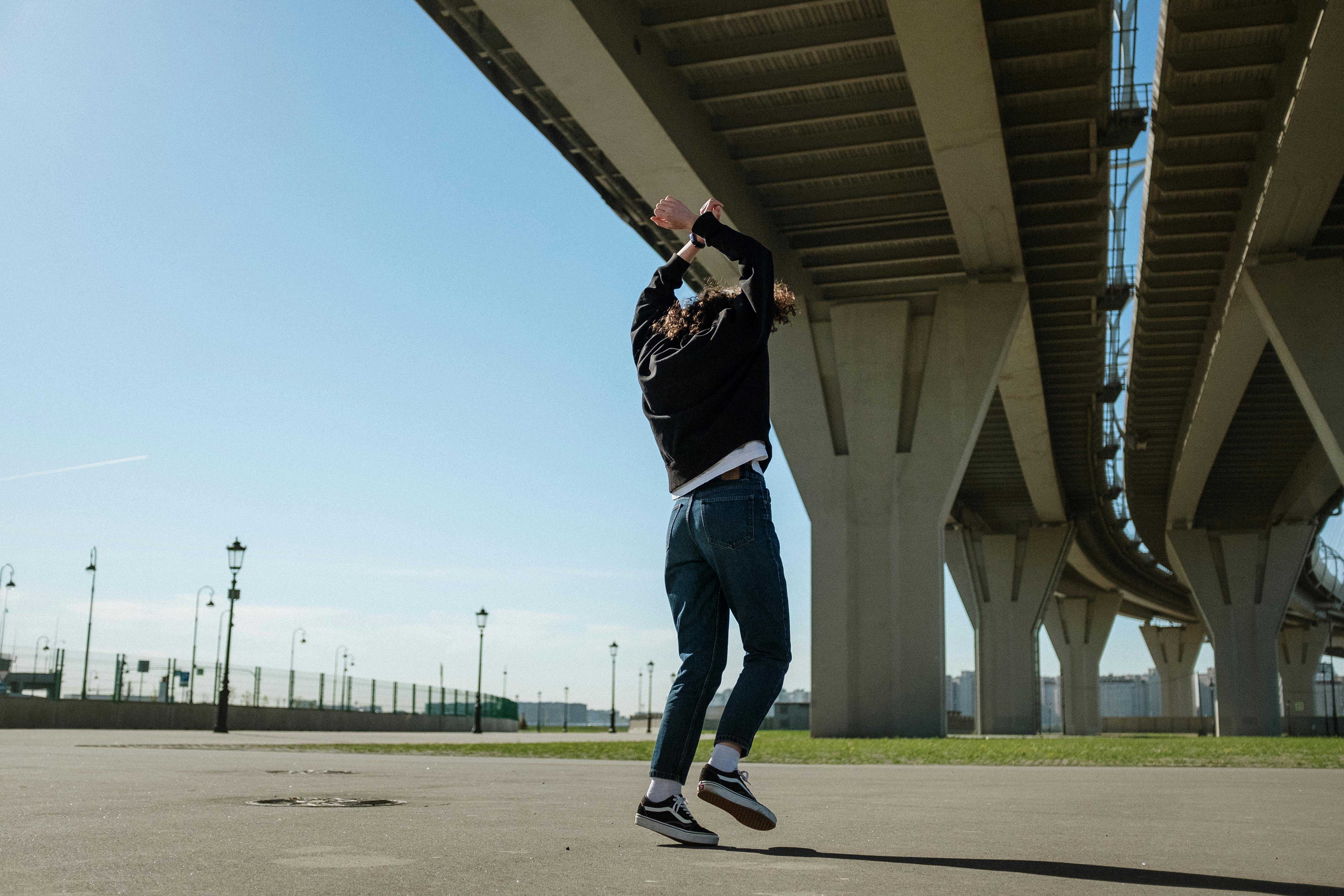 阳光明媚的日子里，一个人在大型城市桥下精力充沛地跳舞