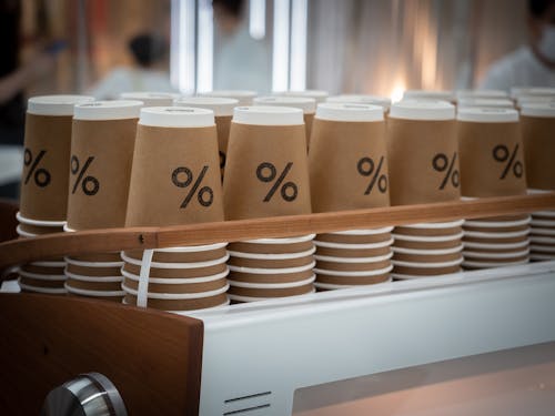 Stack of similar disposable cups with printed percent sign placed on counter in modern coffee shop