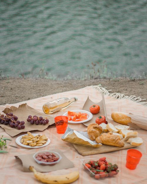 Free Enjoy a serene riverside picnic with fresh fruits, croissants, and refreshing drinks on a cozy blanket. Stock Photo