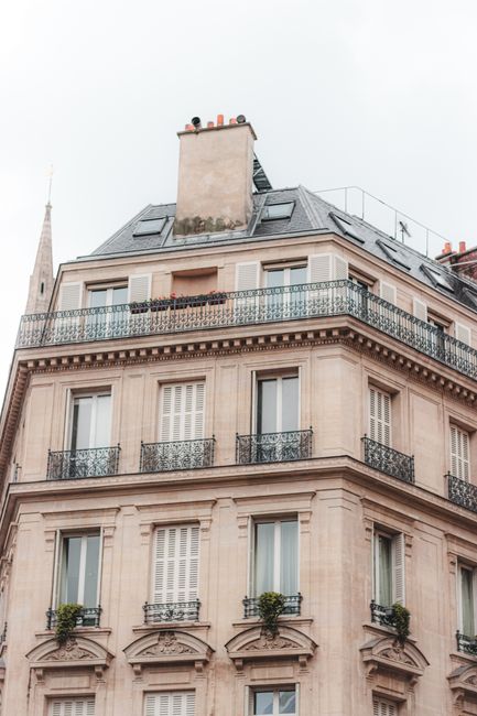 Grey cloudless sky above high beige multi storey construction with simple balconies decorated with pot plants