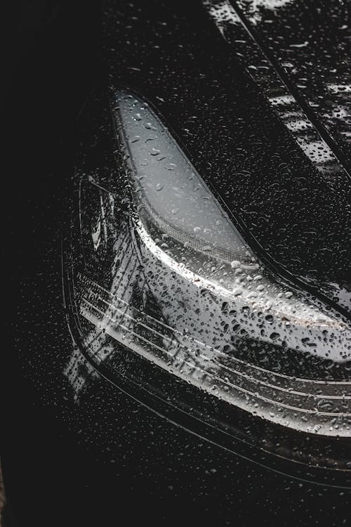Black and white of round tiny transparent drops of rain on surface of headlamps and bumper of contemporary luxury car
