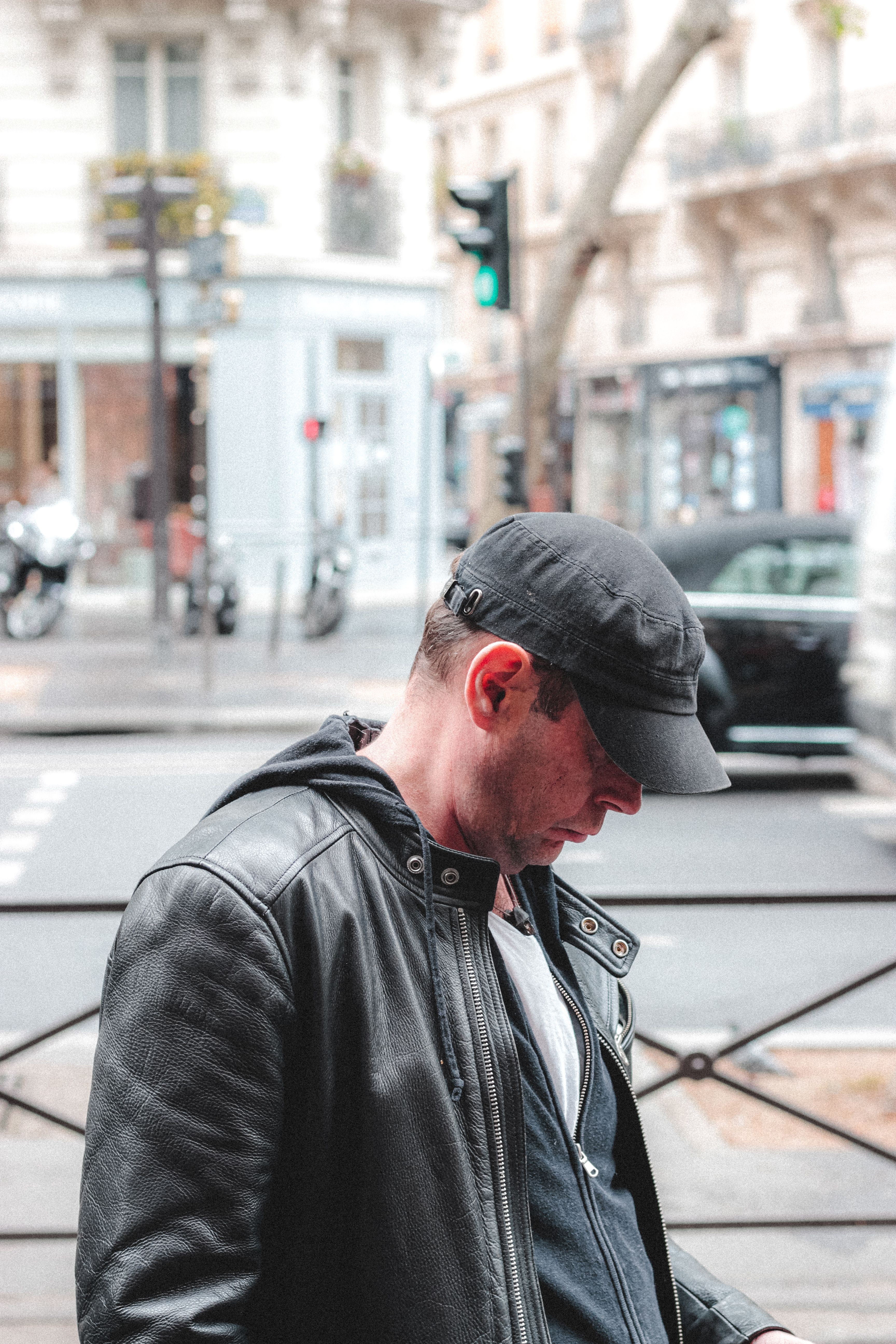Side view of unrecognizable thoughtful adult male in black leather coat and hat looking down in street near zebra crossing in daylight