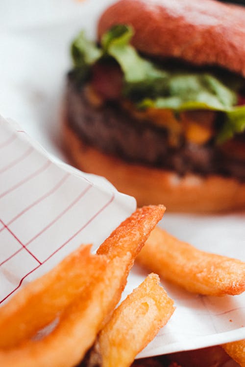 Appetizing light brown French fries and big hamburger with cutlet and lettuce on white crumpled piece of paper