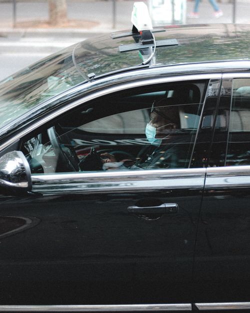 Free Side view of African American male driver in mask driving black taxi on road in downtown of big city at  daytime Stock Photo
