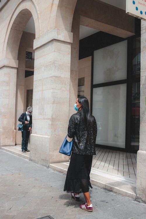 People in protective masks on paved street of old town with concrete building