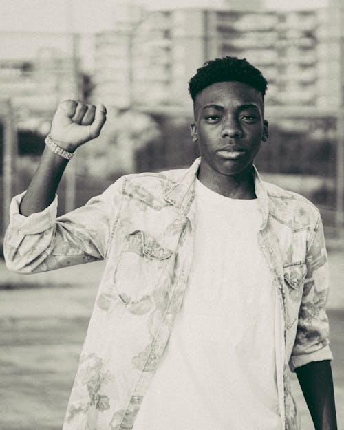 Black and white shot of black young confident man with fist up standing on street