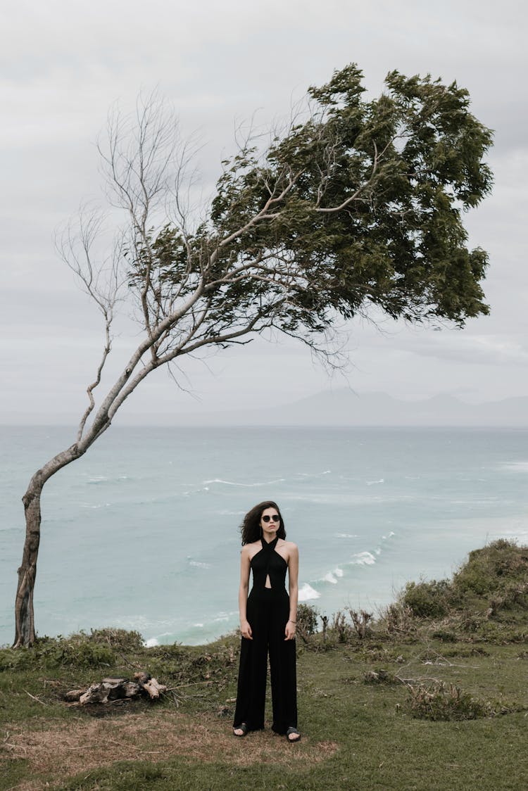 Stylish Woman On Seashore Near Bent Tree