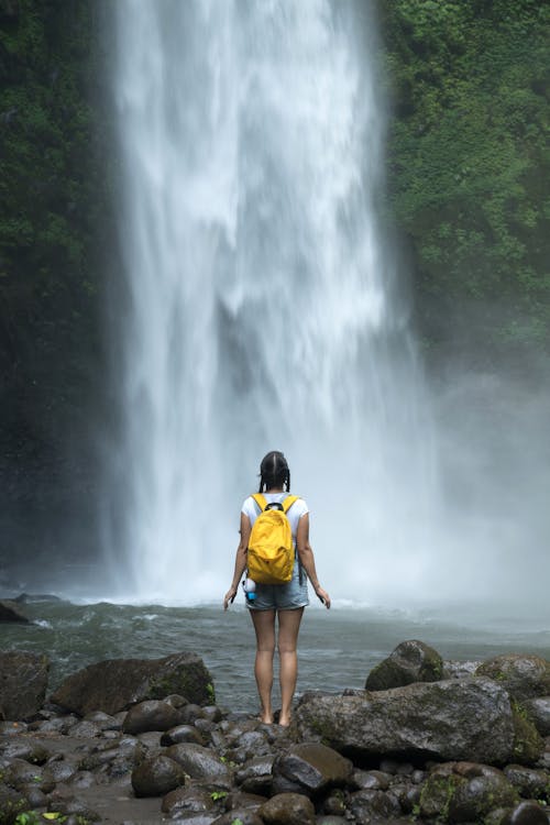 Female backpacker enjoying waterfall streaming from green hills