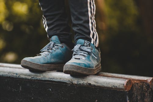 Crop anonymous male in dirty sneakers standing on wooden fence against blurred park