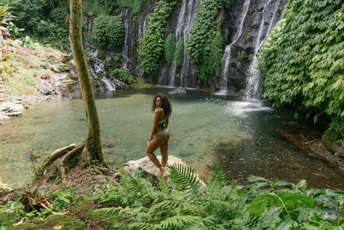 Calm ethnic woman admiring tropical rainforest with waterfall and pond