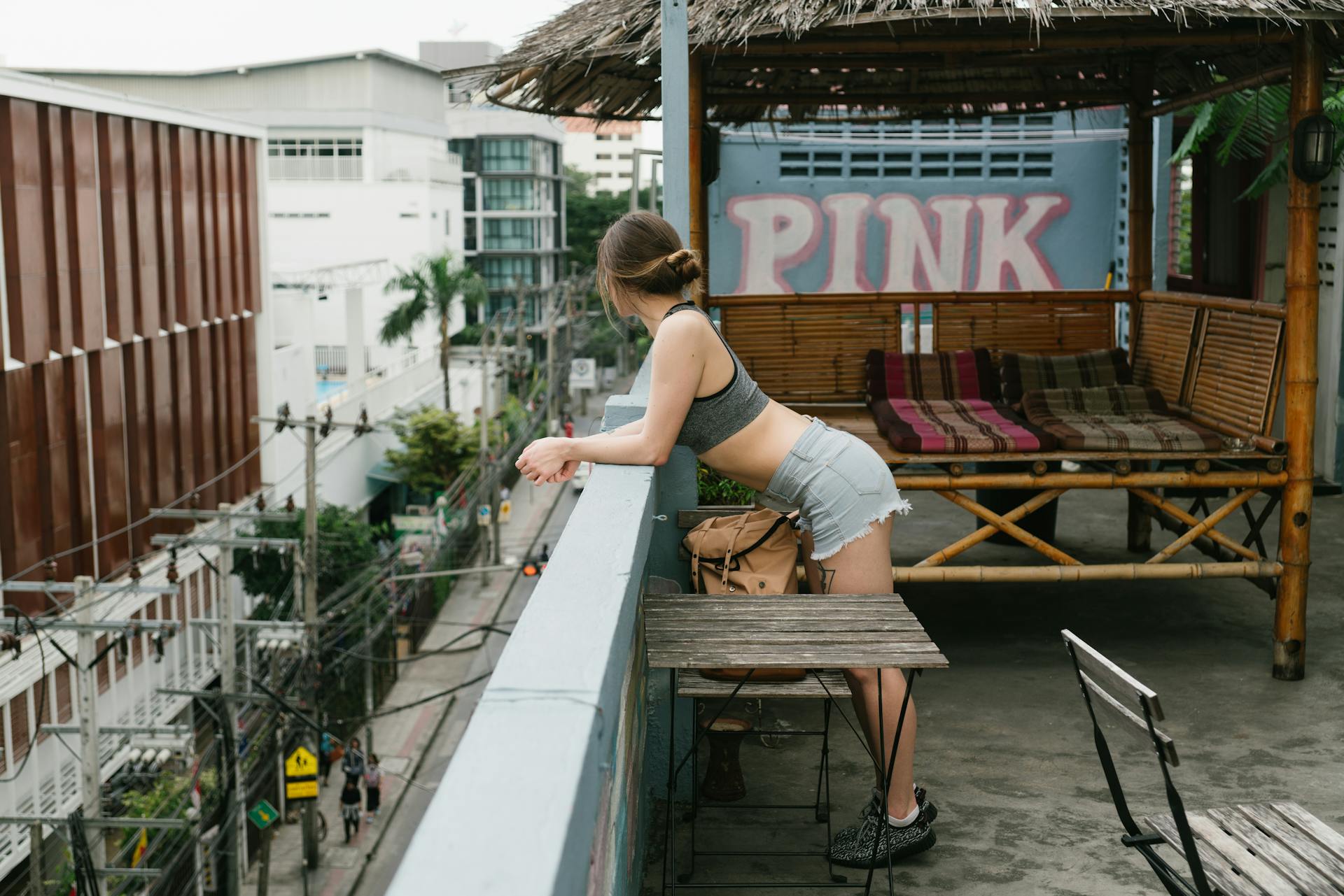 A young woman leans on a balcony railing, enjoying urban views from a rooftop café during summer.