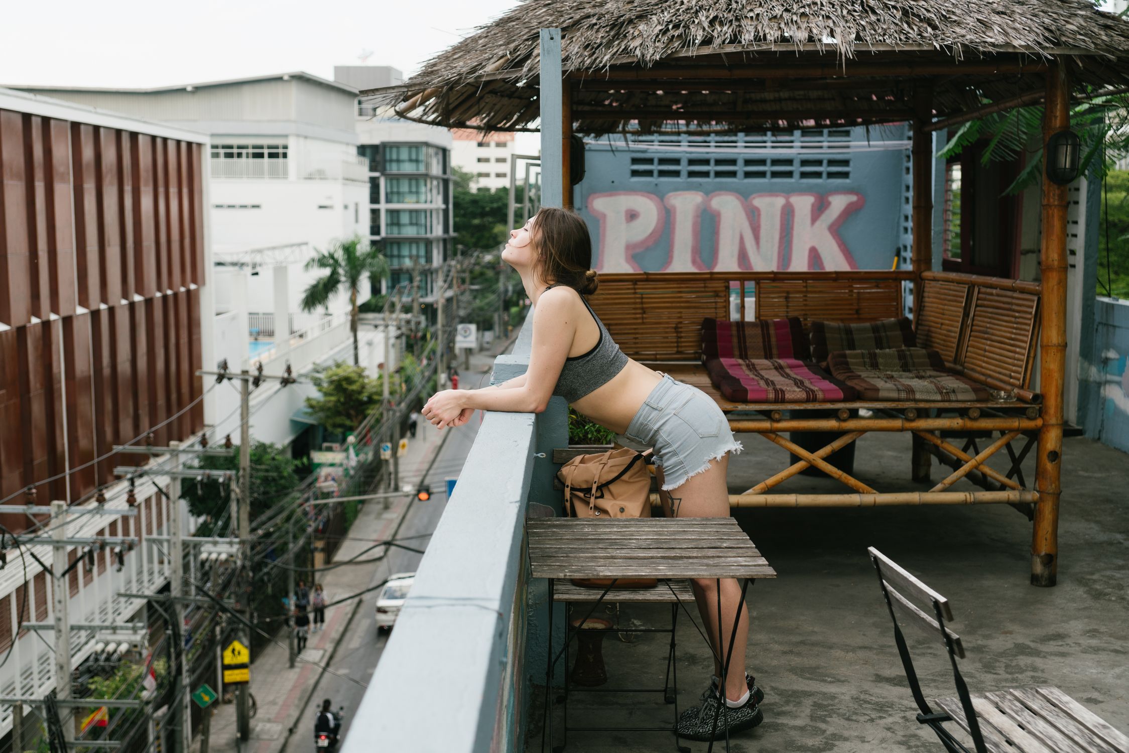 A young woman leans over a rooftop terrace railing in an urban setting, surrounded by city views.