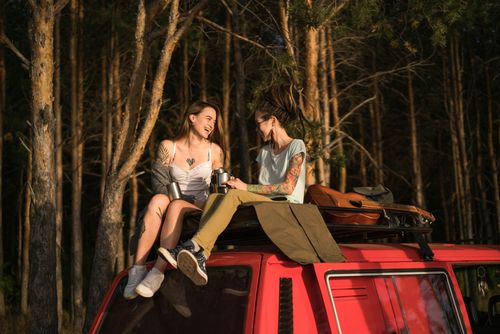 Free Two women laughing and enjoying a scenic sunset on a car roof in the forest. Stock Photo