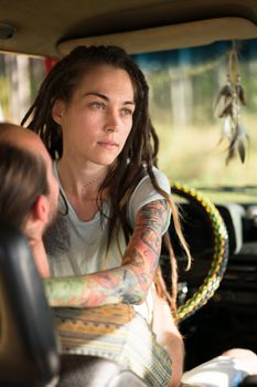 Young couple sitting in car, woman's artistic tattoos visible, serene moment.