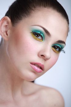Close-up portrait of a woman with striking colorful makeup and a serene expression.