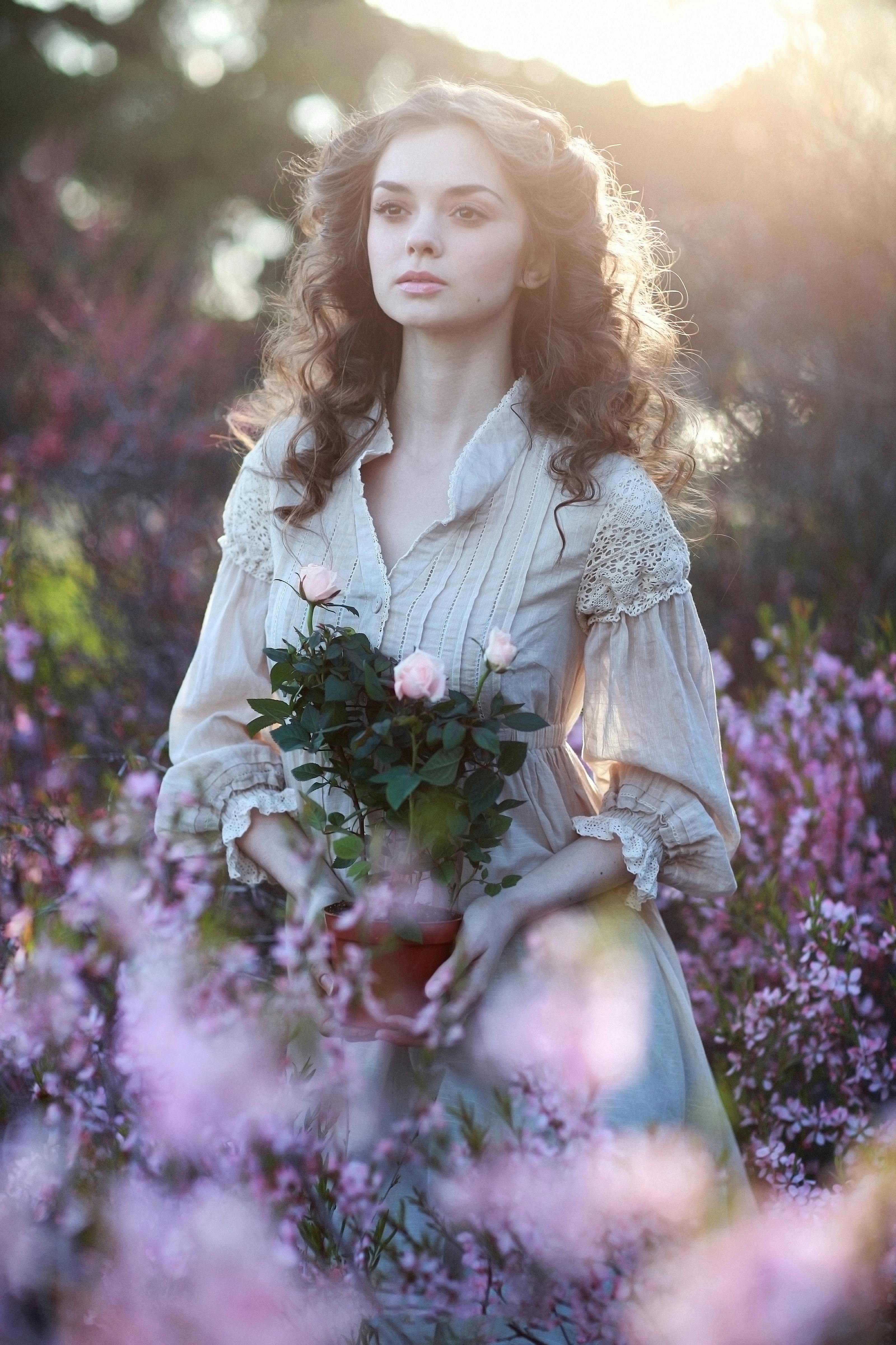 Elegant woman in vintage dress holding roses in a sunlit garden.
