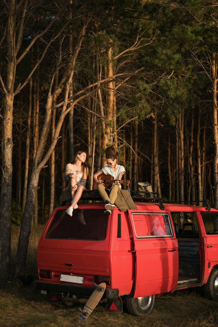 Woman Sitting On Car Roof On Camping And Playing Guitar