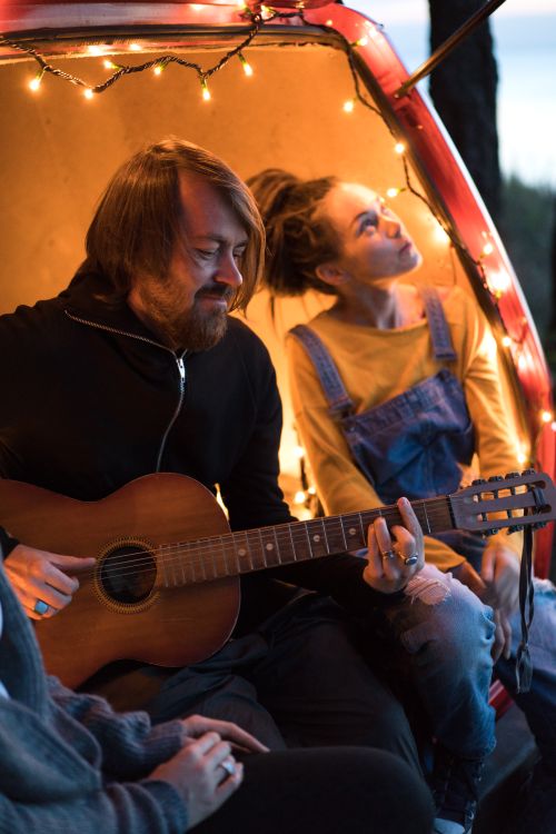 Free Man plays guitar in a van with friends during a cozy evening outing. Stock Photo