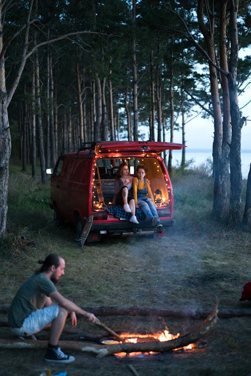 Free A Man Sitting Near the Bonfire while the Two Girls Sitting on the Van Stock Photo
