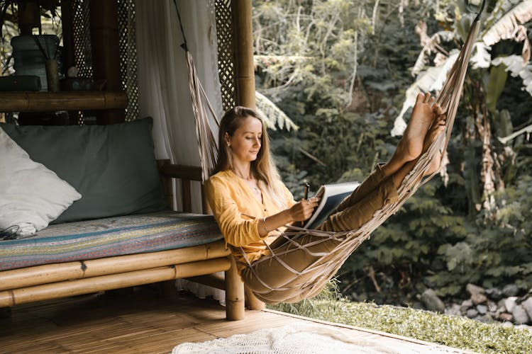 A Woman Sitting On A Hammock While Holding A Sketchbook