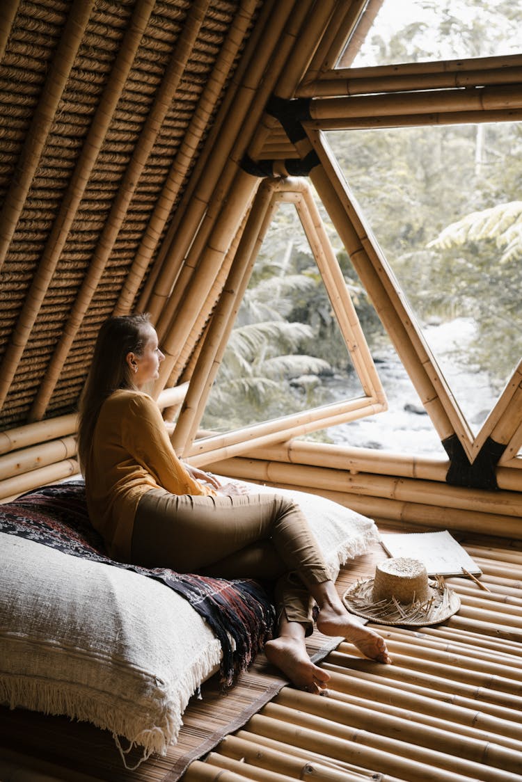 A Woman Sitting On A Cushion While Looking At The Window