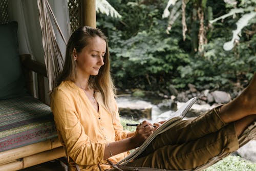 Free A Woman Chilling on a Hammock while Holding a Pen and Sketchbook Stock Photo