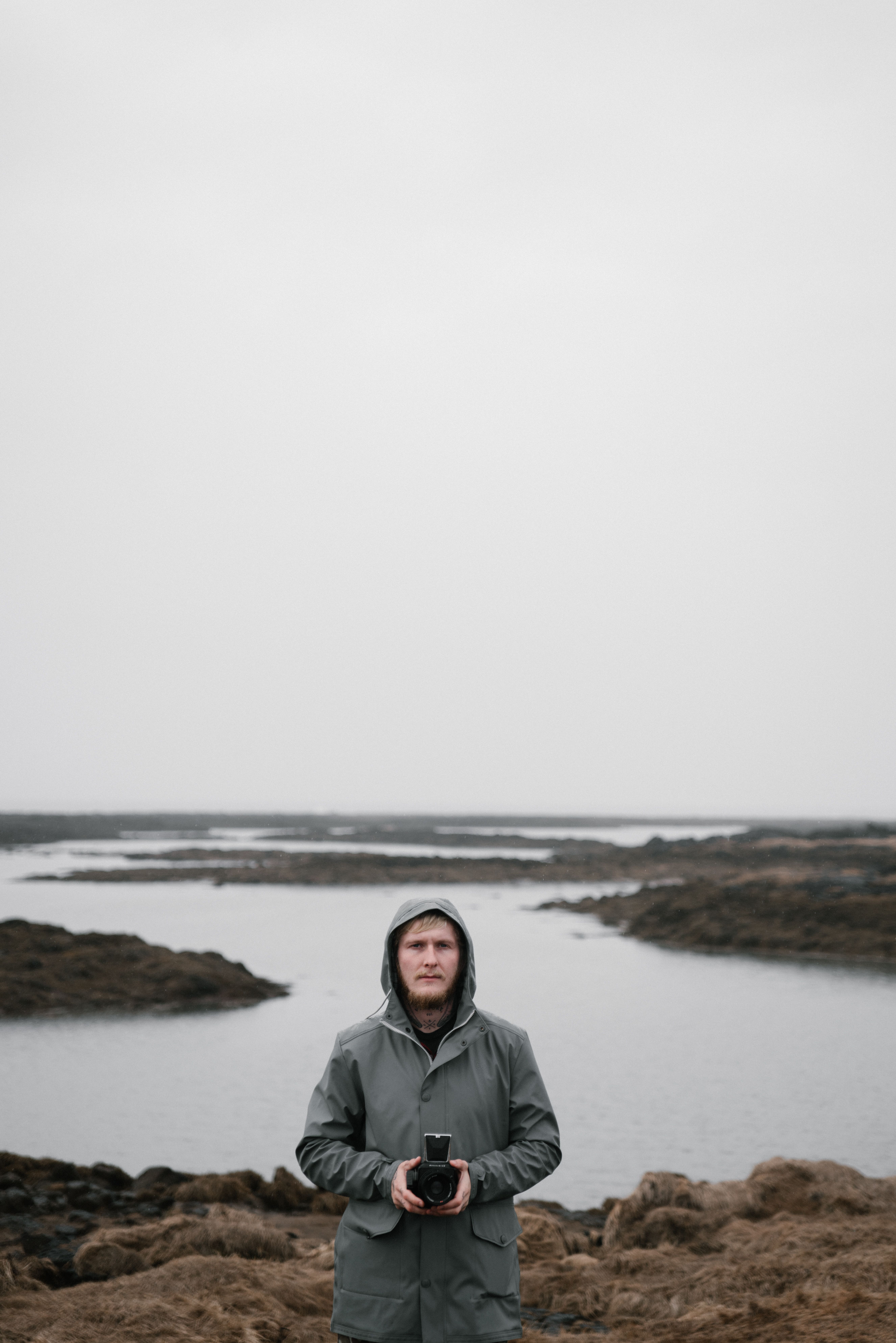 A man in a hooded jacket stands by a misty lake, showcasing solitude and nature.