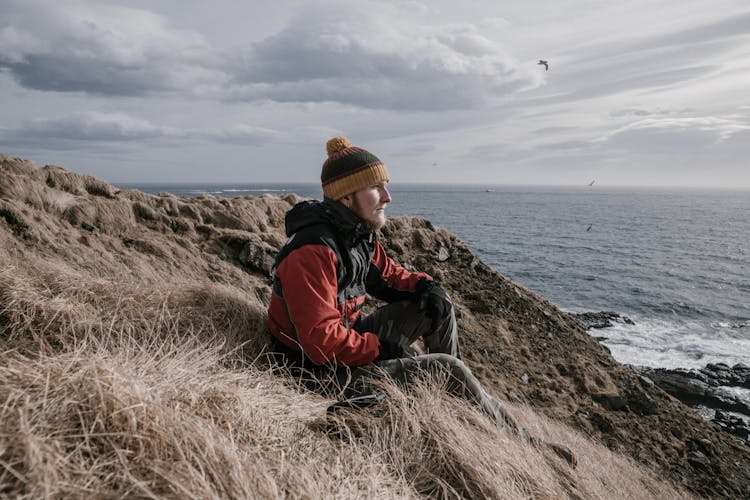 A Side View Of A Man Sitting On A Dried Grass While Looking At The View