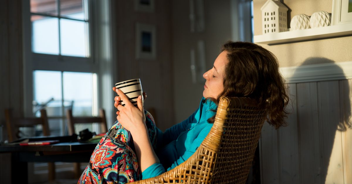 person sitting quietly by a window at sunrise, holding a mug, with a calm expression