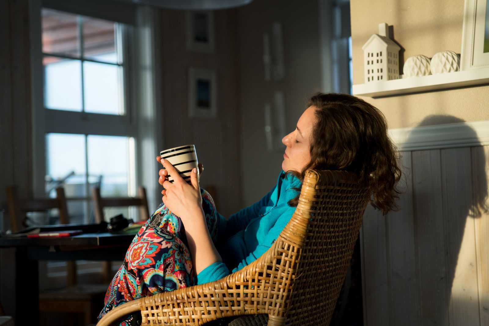 A woman enjoys a quiet moment with coffee, sitting on a rattan chair bathed in natural light.